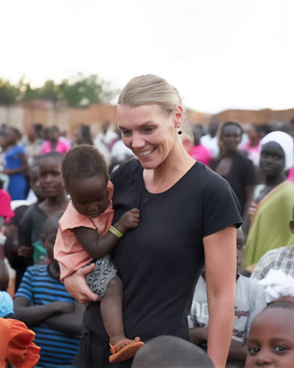 Testimonial afbeelding van Tine Buis met een groep van Afrikaanse kinderen en een kleine peuter in haar armen.